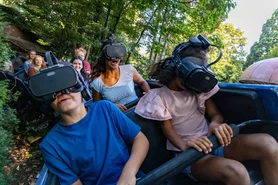 Passengers on Alpine Express ‘Enzian’, four people wearing VR glasses in front, surrounded by green countryside.