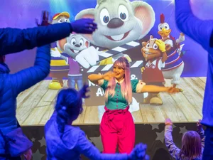 In den kunterbunten JUNIOR CLUB Studios tanzen Kinder mit einer Animateurin vor einer Leinwand mit den Europa-Park Maskottchen.
