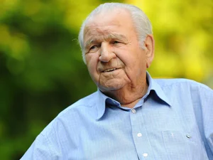 Franz Mack in the sunshine wearing a checked shirt and a friendly smile A smiling Franz Mack in a checked shirt against a sunny, green backdrop with a blurred background.