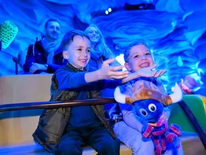 Kinder sitzen gemeinsam mit ihren Eltern und einem Snorri Plüschtier in der Attraktion Snorri Touren im Europa-Park. 