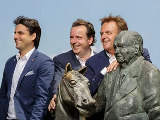 The men of the Mack family gather around the statue of Franz Mack in the sunshine. Statue of Franz Mack with Roland, Michael and Thomas Mack on a sunny day under a blue sky.