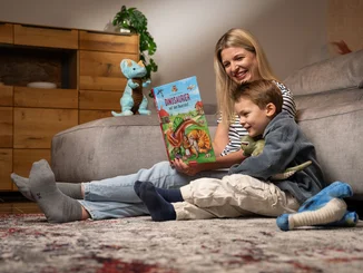 Die Madame Freudenreich Kinderbuchreihe Mutter sitzt neben ihrem kleinen Sohn und liest ihm aus dem Madame Freudenreich Kinderbuch vor.