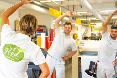 Zwei Europa-Park Mitarbeiter in der Werbetechnik machen eine Dehnungsübung mit einem FeelGood Trainer.