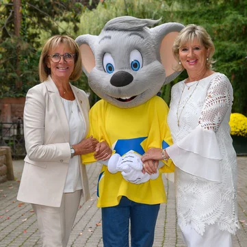 Marianne and Mauritia Mack together with Ed Euromaus in a natural setting. Marianne and Mauritia Mack with Ed Euromaus against a backdrop of trees and flowers.