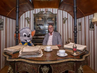 Roland Mack in a circus wagon Roland Mack sits at a desk in a historic circus wagon with a large Ed soft toy.