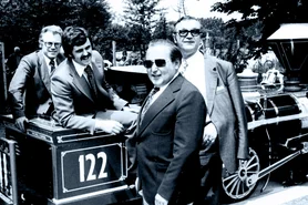 Roland Mack sits laughing on the locomotive of the Panorama Train, surrounded by important guests.