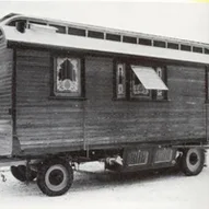 Photo noir et blanc d'une caravane conçue avec art par l'atelier de construction de chariots Mack Roulotte historique aux fenêtres décorées.