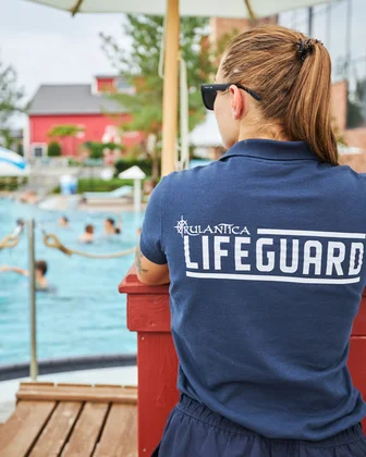 Un maître-nageur surveille la baignade dans l’univers aquatique Rulantica. Une maître-nageuse, avec des lunettes de soleil et un t-shirt « lifeguard » observe la zone de baignade à Rulantica.