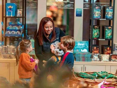 Shopping Europa-Park Une collaboratrice d’une boutique de souvenirs à Europa-Park présente une peluche Ed Euromaus à deux enfants, ravis.