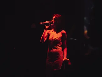 Exklusive Auftritte nur für Sie Eine Frau singt im Dunklen, sie wird nur von einer Lampe beleuchtet.