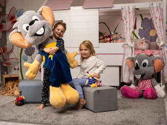 Ed & Edda für zu Hause Zwei Kinder in ihrem Kinderzimmer haben große Plüsch-Euromäuse, mit denen sie spielen.